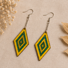 Load image into Gallery viewer, Aurora Step wooden earrings arranged on neutral linen, showing the vivid yellow wood, green resin geometric accents, silver-tone chains and hooks.