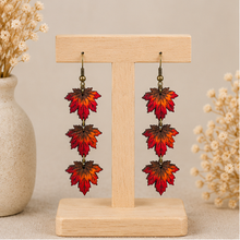 Cargar imagen en el visor de la galería, Autumn Ember hand-painted wooden earrings displayed front-facing on a light wood stand.
