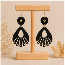 Load image into Gallery viewer, Ebony Moon wooden earrings shown from the reverse side on a light wood stand, showing the same black-and-gold design on both sides.