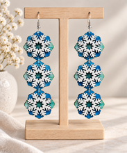 Load image into Gallery viewer, Frozen Sky layered snowflake wooden earrings in blue, icy green and white on a light wood stand