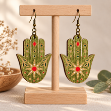 Load image into Gallery viewer, Mystical Hamsa Hand double-sided wooden earrings on a light wood stand with hand-painted green, red, gold, and white details