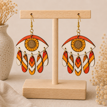 Load image into Gallery viewer, Radiant Eye hand-painted wooden earrings displayed front-facing on a light wood stand.