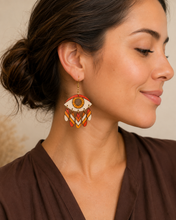 Load image into Gallery viewer, Radiant Eye hand-painted wooden earring shown at realistic scale on a model wearing a warm cocoa blouse.
