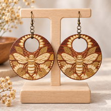 Load image into Gallery viewer, Sunset Honey Bee engraved wooden earrings with bee and sunflower design on a light wood stand with hypoallergenic bronze-tone hooks