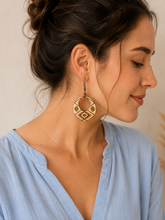 Load image into Gallery viewer, Model wearing Tribal Spirit engraved wooden earrings with a soft dusty-blue blouse, showing a realistic medium scale and natural wood finish.