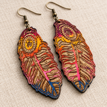 Cargar imagen en el visor de la galería, Close detail view of boho feather wooden earrings highlighting intricate laser engraving, hand-painted sunset colors, natural wood grain and bronze-tone hooks.
