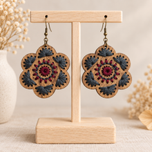 Load image into Gallery viewer, Crimson Roots embroidered wooden earrings displayed front-facing on a light wood stand against a warm cream background.
