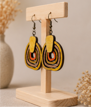 Load image into Gallery viewer, Angled view of Earth Echoes hand-painted wooden earrings on a light wood stand.
