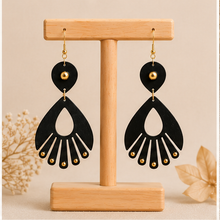 Load image into Gallery viewer, Ebony Moon wooden earrings shown from the front on a light wood stand, with deep black hand-painted wood and small gold-tone accents.

