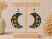 Load image into Gallery viewer, Hand-painted Enchanted Forest Moon wooden earrings displayed front-facing on a light wood stand.
