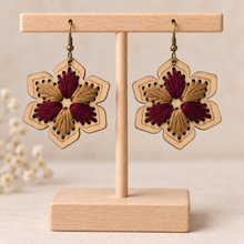 Load image into Gallery viewer, Hand-embroidered floral wooden earrings in burgundy and warm camel on a light wood stand

