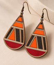 Load image into Gallery viewer, Close angled view of geometric teardrop wooden earrings showing hand-painted orange, deep red and dark sections, engraved lines, natural wood grain and bronze-tone hooks.
