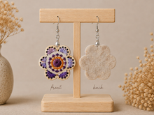 Load image into Gallery viewer, Lavender Bloom hand-embroidered wooden earrings shown front and back on a light wood stand, with the felt-backed reverse visible.
