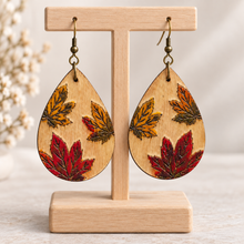 Load image into Gallery viewer, Leaf Whispers engraved wooden earrings with hand-painted autumn leaves on a light wood stand
