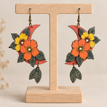 Load image into Gallery viewer, Moon Flower layered wooden earrings on a light wood stand with hand-painted orange and yellow flowers
