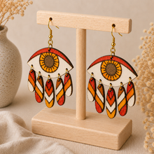 Load image into Gallery viewer, Radiant Eye hand-painted wooden earrings shown at an angle on the standard light wood stand, highlighting the layered dangling construction.
