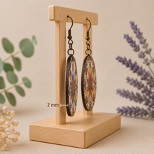 Cargar imagen en el visor de la galería, Side profile of reversible mandala wooden earrings on a light wood stand showing the 2 mm wood thickness.
