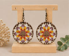 Cargar imagen en el visor de la galería, Reversible mandala wooden earrings on a light wood stand showing the yellow and coral mandala side.
