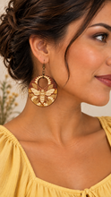 Load image into Gallery viewer, Model wearing Sunset Honey Bee lightweight wooden earrings with engraved bee and sunflower design, bronze-tone hooks, and a medium yellow top
