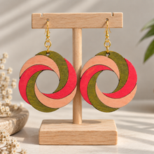 Load image into Gallery viewer, SunTwist Joy hand-painted wooden swirl earrings in coral, peach and olive on a light wood stand with gold-tone hooks
