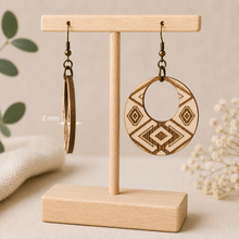 Load image into Gallery viewer, Side view of Tribal Spirit engraved wooden earrings on a light wood T-stand, showing the 2 mm American linden wood thickness beside a front-facing earring.
