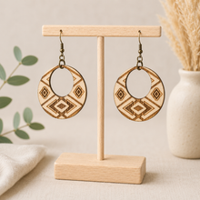 Load image into Gallery viewer, Tribal Spirit engraved wooden earrings displayed front-facing on a light wood T-stand, showing natural American linden wood grain and bronze-tone hooks.
